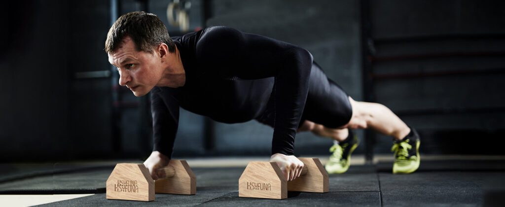 hombre haciendo calistenia en su casa con paralelas resistentes de madera para pectoral